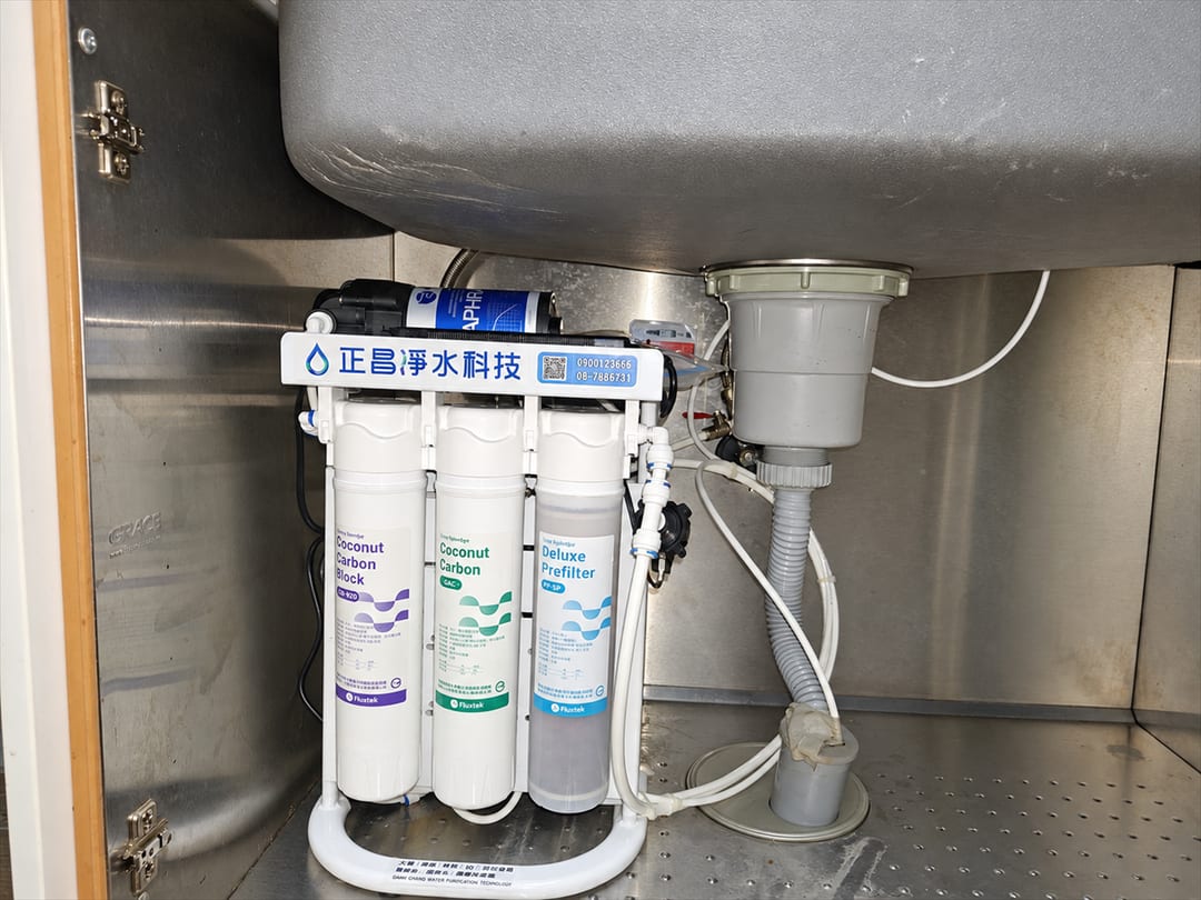 不鏽鋼廚櫃裡的直輸型 RO 主機，三支濾心並排，旁邊是排水管